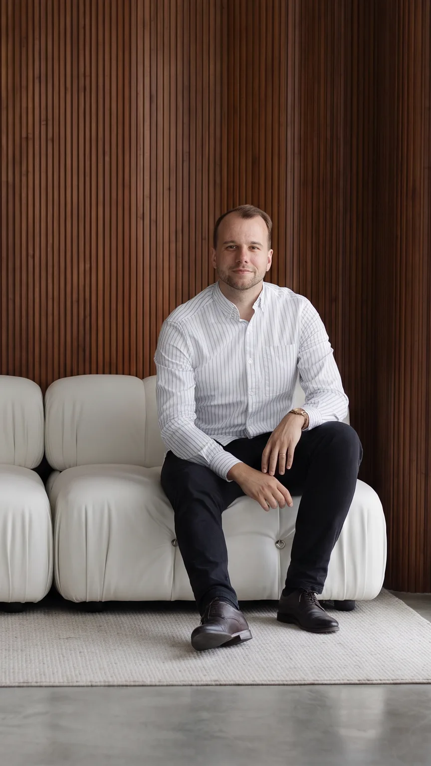Chris P. sitting on a white sofa in a sunlit room with a slatted walnut wall behind him