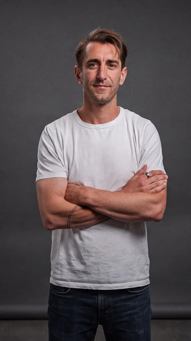Joel Martin standing with arms crossed in a white t-shirt against a dark grey studio backdrop